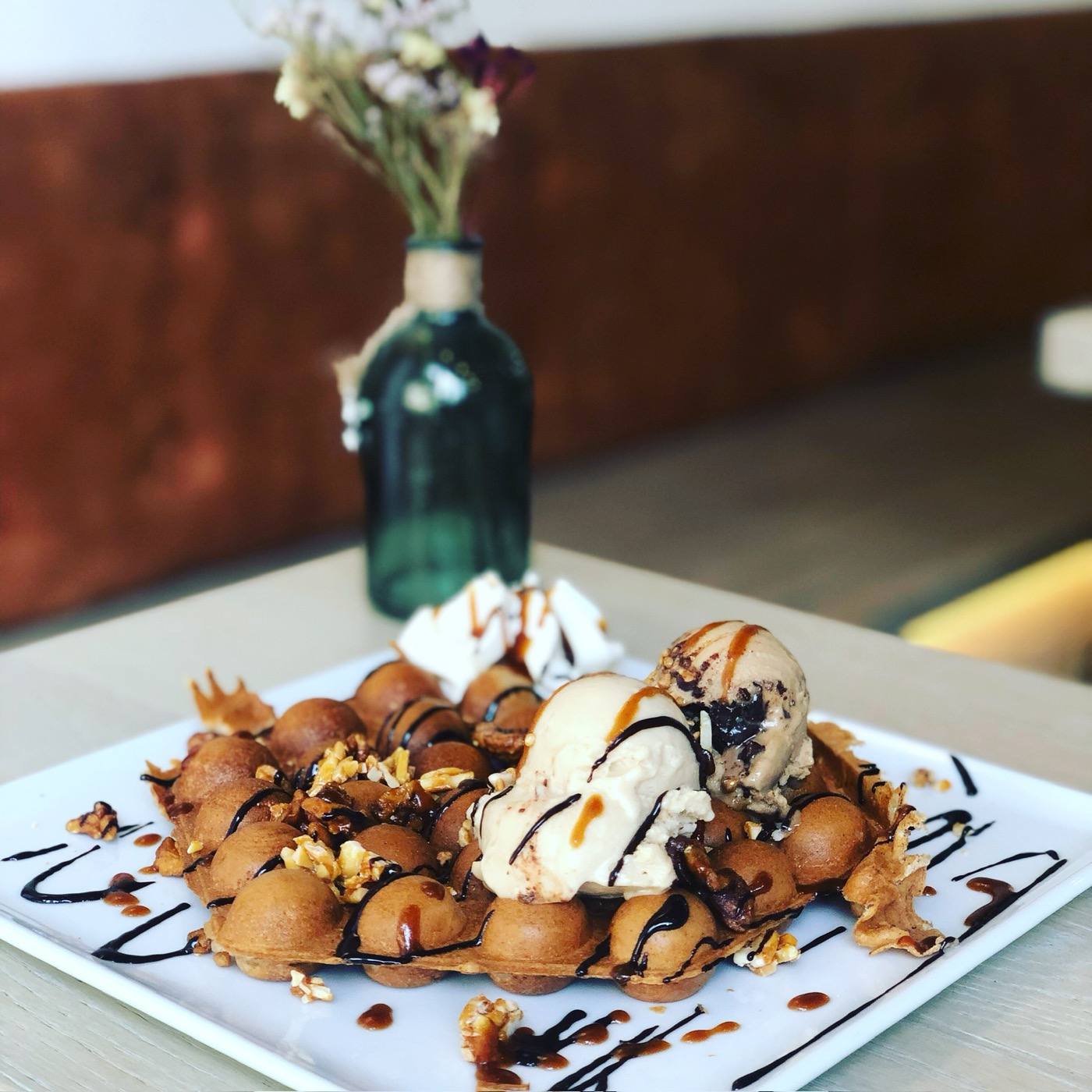 Bubble Waffle auf dem Teller mit Eis, Karamellsauce und Nüssen