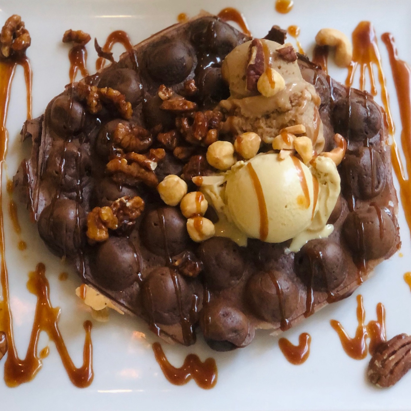 Schoko-Bubble-Waffle flach auf dem Teller mit Eis, Nüssen und Karamellsauce