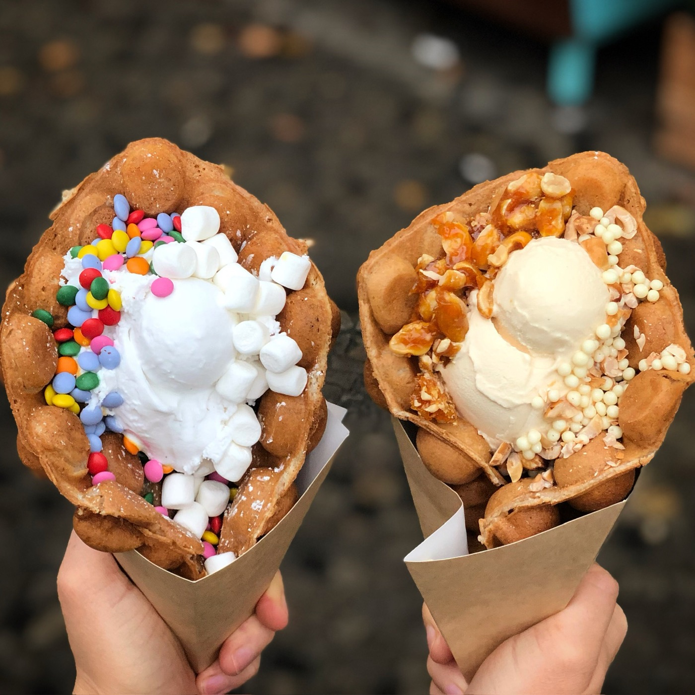 Zwei Bubble Waffles in Papiertüten: mit Marshmallows und Schokolinsen sowie mit Eis und Krokant